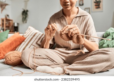 Sunlit closeup of young African American woman knitting handmade piece while sitting on couch at home and enjoying cozy hobby