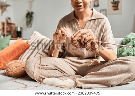Sunlit closeup of young African American woman knitting handmade piece while sitting on couch at home and enjoying cozy hobby