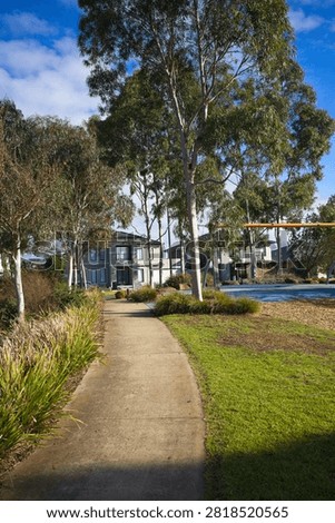 Sunlit concrete walking path wind through native gum trees with modern two-storey family homes visible in the background at Bullion Park, Woodlea Estate in Aintree.
