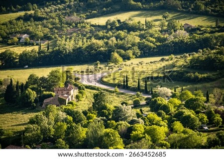 Sunlit fields, forests and vineyards featuring a farmhouse and snaking road – panoramic vista over the countryside in Provence, France