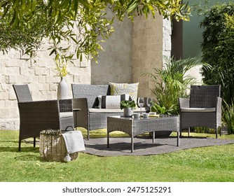 Sunlit garden dining space, a rattan weave furniture set, two armchairs and a sofa with neutral cushions, a coffee table against a textured stone wall backdrop, refreshing morning meal lush greenery. - Powered by Shutterstock