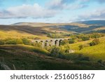 A sunlit landscape in Dentdale, Yorkshire Dales with a ruined barn and viaduct in the distance, Yorkshire Dales, England, United Kingdom