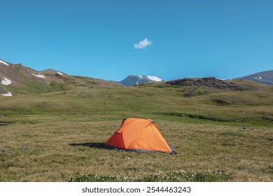 Sunlit orange tent on alpine grassy glade near white flowers of dryas among green rocky hills against snow mountain top under one small cloud in blue sky in sunny day. High mountains in bright sun. - Powered by Shutterstock