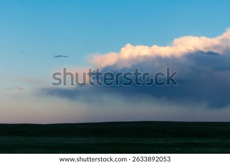 A Sun-lit Rain Cloud over Flat Prairie Land at Sunset