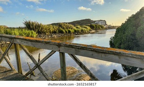 Sunlit rustic bridge over tranquil estuary, whispers of Celtic twilight, invoking Lughnasadh serenity and coastal wanderlust allure