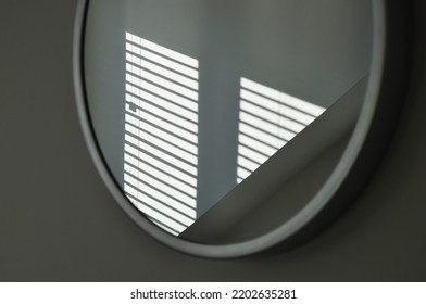 Sunlit Shadow From A Venetian Blind Window Shutter Reflected In A Round Mirror On A Grey Wall. Minimalist Zen Like Modern Abstract Monochrome Interior Design Element. Stylish, Elegant And Enigmatic.