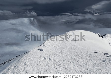 Sunlit snow covered mountain summit above dramatic dark clouds in severe weather, Mount Elbrus, Caucasus, Russia