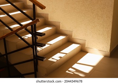 Sunlit staircase with railings in the house. Staircase at the entrance of an apartment building. Modern entrance interior in living complex. Shadow and light.  - Shutterstock ID 2044349678