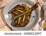 Sunlit Still Life of Pan-Fried Flounder with Lemon Wedge on Beige Table.