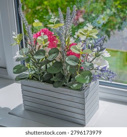 Sunlit window sill holds a rustic grey planter. Pink hydrangeas and purple lavender add vibrant color. Green eucalyptus leaves frame the floral arrangement. Soft natural light enhances textures