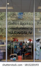 Sunne, Sweden Sept 11, 2020 A Man Reads A Newspaper In The Local Library. Sign Says In Swedish Geneology, And Industry.