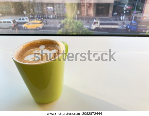 Sunny afternoon, drinking coffee with a green cup\
with a crying bear latte art, sitting in front of the glass window,\
looking at the busy street scene, cars, taxi, trucks and vans\
shuttled on the road