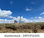 A sunny archaeological excavation in the Badlands with flags, shovel, screen, tarp, and cutbank.