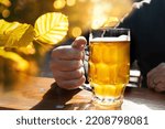 Sunny autumn day in the beer garden. Guest with fresh filled beer mug in the hand and golden autumn leaves in the background.