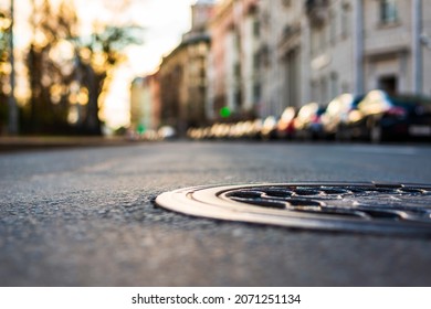 Sunny autumn day. A row of parked cars on the street. The road after the rain. Focus on the manhole cover. Close up view of a manhole cover at the level of the asphalt.