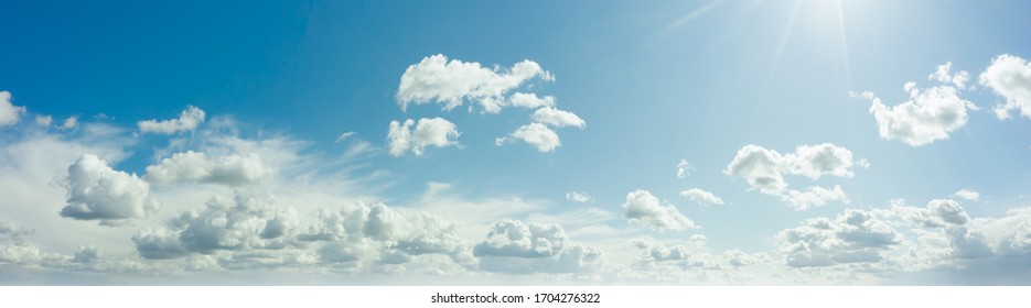 Sunny blue sky with fluffy clouds. Sunlight with rays illuminates the sky. Beautiful ultra-wide panoramic background of atmosphere.
