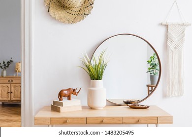 Sunny boho interiors of apartment with mirror, dressing table, furnitures, flowers, plants, rattan hat, sculpture, macrame and design accessories. Stylish home decor of open space. Template.