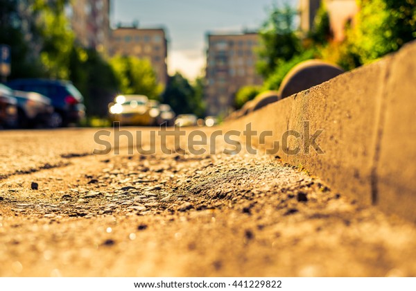 Sunny day in a city, bad road in city courtyard\
with parked cars. View from the curb level, image in the\
yellow-blue toning