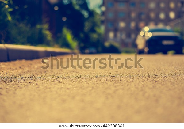 Sunny day\
in a city, bad road in city courtyard with parked cars. View from\
the curb level, image in the yellow\
toning