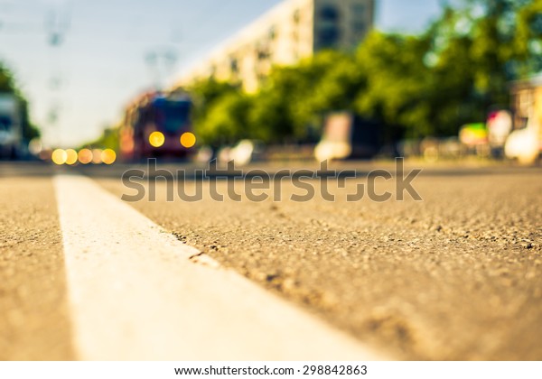 Sunny day in a city, tram rides on rails next to\
the stream of cars, the view from the level of asphalt. Image in\
the yellow-blue toning