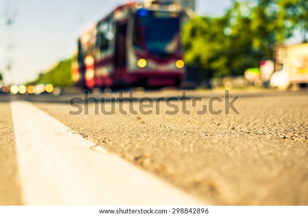 Sunny day in a city, tram rides on rails next to
the stream of cars, the view from the level of asphalt. Image in
the yellow-blue toning