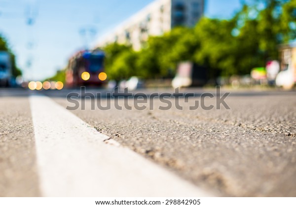 Sunny day in a city, tram\
rides on rails next to the stream of cars, the view from the level\
of asphalt