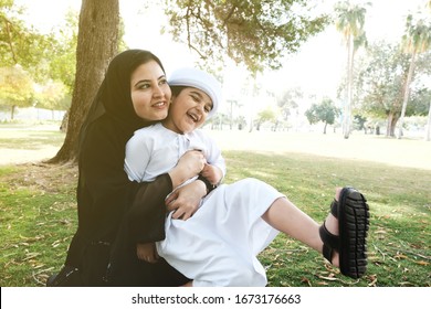 Sunny Day With Emirati Mother And Son. Arab Woman On Abaya Hijab With Arabic Emirati Boy Child During Sunny Outdoor. Lifestyle Shot Of Emirati Family