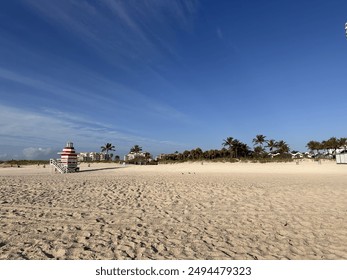 Sunny day at Miami Beach with a red-and-white striped lifeguard tower and palm trees in the distance, showcasing the wide sandy beach and clear blue sky. Perfect for travel, nature, and coastal themes - Powered by Shutterstock