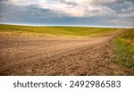 Sunny day on a dirt road through picturesque countryside with green fields under a cloudy sky