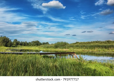 Sunny day over river bank, wooden pier for boats, blue sky with clouds above it. - Shutterstock ID 791977717