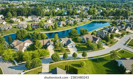 Sunny day over suburban neighborhood with long manmade pond between houses aerial