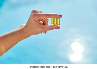 Sunny Golden Vitamin D Oil Capsules Omega-3 In Woman Hand, Background Sun Blue Water. Healthy Lifestyle, Nutritional Supplements, Diet