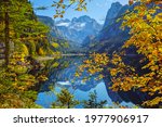 Sunny idyllic colorful autumn alpine view. Peaceful mountain lake with clear transparent water and reflections. Gosauseen or Vorderer Gosausee lake, Upper Austria. Dachstein summit and glacier in far.