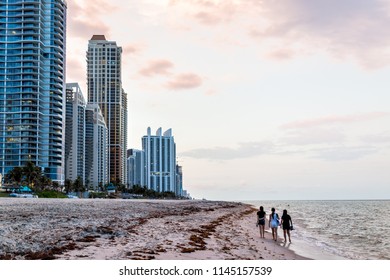 Sunny Isles Beach, USA - May 7, 2018: Apartment Condo Hotel Buildings During Vintage Sunset Evening In Miami, Florida With Skyscrapers Urban Sand, Waves Crashing On Shore Coastline, People