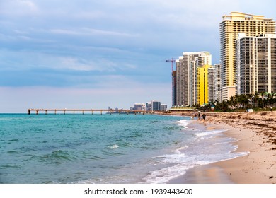 Sunny Isles Beach, USA - May 7, 2018: Apartment Hotel Or Condo Buildings Skyscrapers At Sunset Evening In Miami, Florida With People By Pier And Waves