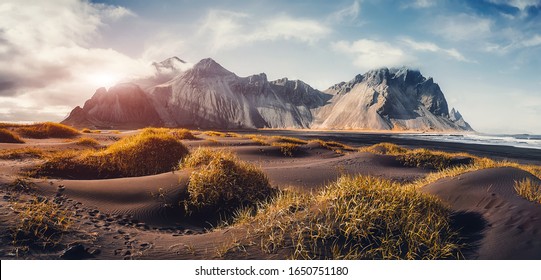 Sunny landscape of Iceland. Gorgeous view on Stokksnes cape and Vestrahorn Mountain with black sand with grass on foreground at summer. Iconic location for landscape photographers. Wonderful nature. - Powered by Shutterstock