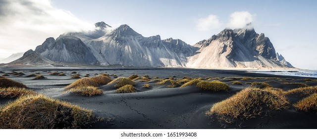 Sunny landscape of Iceland. Gorgeous view on Stokksnes cape and Vestrahorn Mountain with black sand with grass on foreground at summer. Iconic location for landscape photographers. Wonderful nature.
