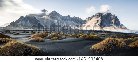 Sunny landscape of Iceland. Gorgeous view on Stokksnes cape and Vestrahorn Mountain with black sand with grass on foreground at summer. Iconic location for landscape photographers. Wonderful nature.
