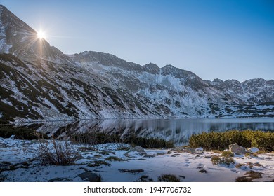 Sunny Morning Of December In High Tatras, Poland. Alpine Climate, Bright Sunrays And Perfect Reflection On The Lake. Selective Focus On The Rocks, Blurred Background.