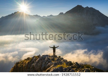 Sunny morning. Happy hiker with hands in the air stand on rock. View over misty and foggy morning valley.