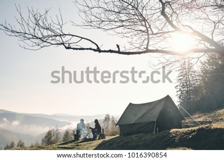 Sunny morning. Young couple having morning coffee while camping in mountains