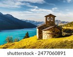 Sunny picturesque view of stone chapel on Roselend lake (Lac de Roselend) in France Alps (Auvergne-Rhone-Alpes). Landscape photography


