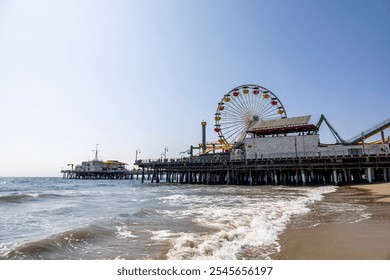 Sunny Santa Monica Pier with Ferris wheel by the ocean under a clear blue sky, waves lapping the shore. - Powered by Shutterstock