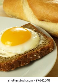 Sunny side up egg on a slice of bread on a plate with a French loaf in the background
