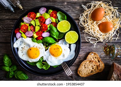 Sunny side up eggs with avocado, cherry tomatoes, toasted bread and red onion on wooden table  - Powered by Shutterstock