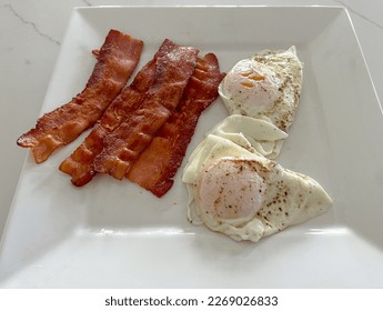 Sunny side up eggs and bacon on a white plate. - Shutterstock ID 2269026833