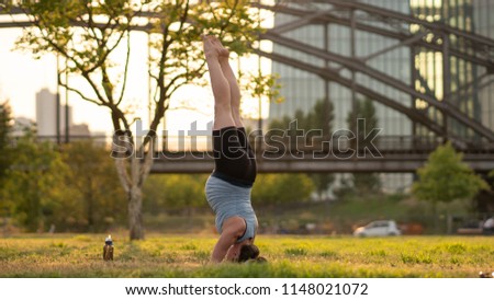 Sunny summer day. Young athletic Pregnant woman doing handstand among modern skyscrapers. Exercise outdoors, workout. Exercise for balance, yoga, training. Healthy lifestyle.