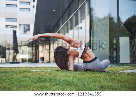 Sunny summer morning. Young athletic woman doing handstand on city park street among modern urban buildings. Exercise outdoors healthy lifestyle.