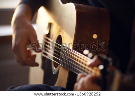 Sunny sunset light illuminates the hands of the guitarist, playing a melody on a wooden six-string acoustic guitar