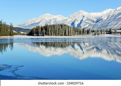 Sunny view of the reflection of mountains in freezing Lac Beauvert in Jasper National Park, Alberta, Canada